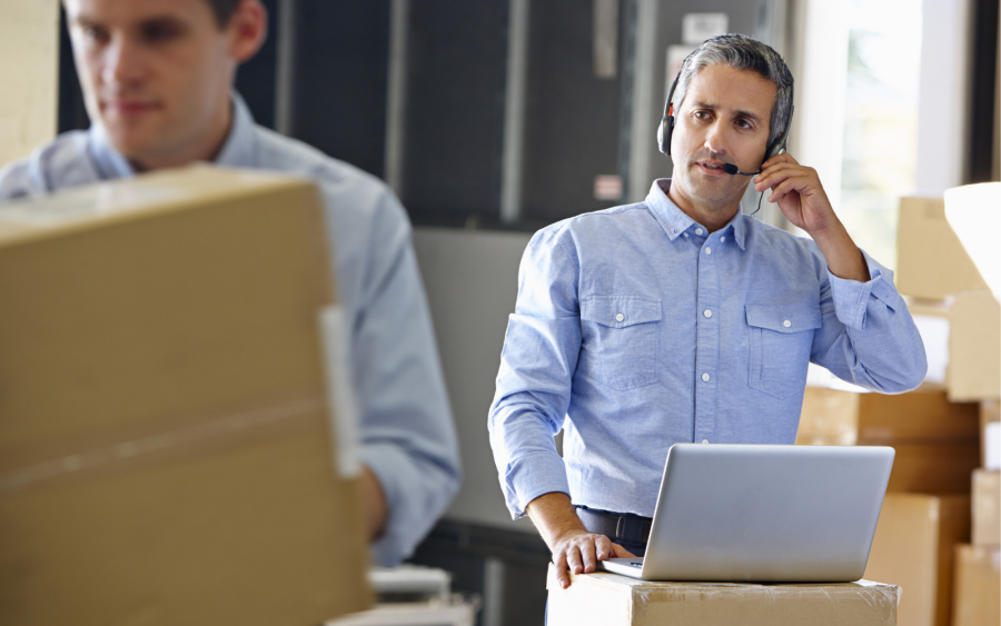 Man wearing headset at laptop in warehouse